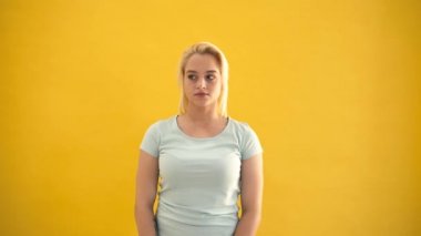 Genç sarışın beyaz artı boyutu modeli sessizlik jesti sarı arka plan gösterir.