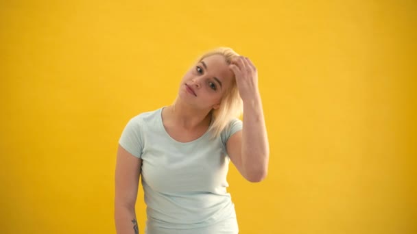 Молодой блондин плюс размер модели выпрямить волосы и смотреть на камеру на желтом фоне — стоковое видео