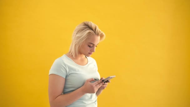 Boyutu sarışın modeli göz kontrol mesaj smartphone vasıl sarı arka plan üzerinde heyecanlı. — Stok video