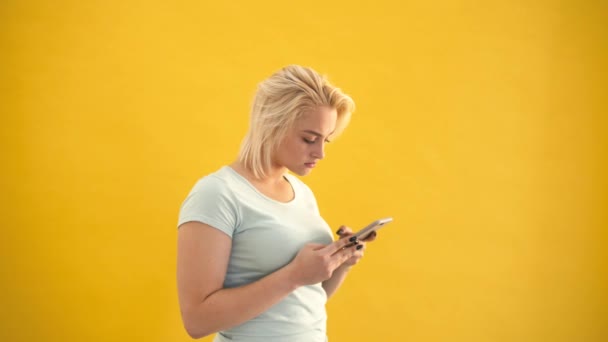 Boldogtalan szőke plus size modell meglepett ellenőrző üzenetet a telefon a sárga háttér — Stock videók