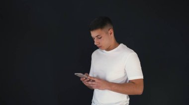 Ciddi adam güzel video standları ve telefon kullanır. O elinde tutar. Aniden adam gülümseme ve gülmek başlar. Sevindi. Genç adam telefonu kullanmaya devam. Siyah arka plan üzerine izole