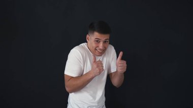 Komik adam anlamına gelir ve kameraya poz veriyor. Genç adam büyük parmaklarını tutar. Adam eğlenceli ruh hali vardır. Siyah arka plan üzerine izole