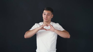Çok güzel ve yakışıklı bir genç adam parmak ile kalp şekli göstermektedir. O çok emindir. Siyah arka plan üzerine izole