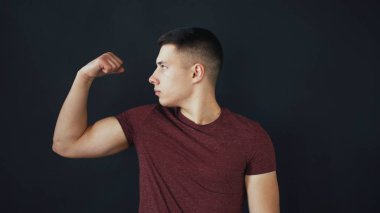 Genç standları ve pozlar adam. O ellerde kas gösterir ve onları öper. Siyah arka plan üzerine izole.