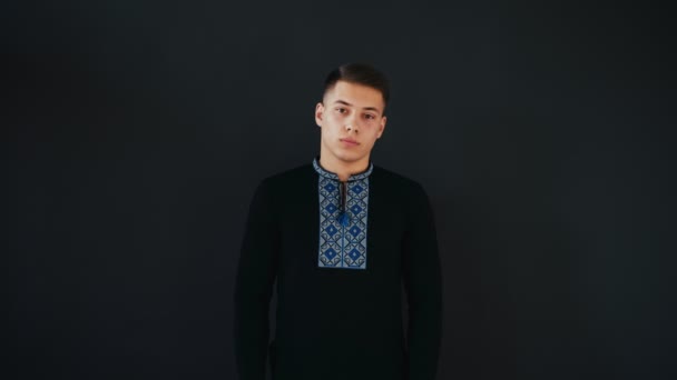 Young man stands in black shirt and looks on camera with confidence. Then guy stars to laugh. At the end he makes playful emotion. Isolated on black background. — Stock Video