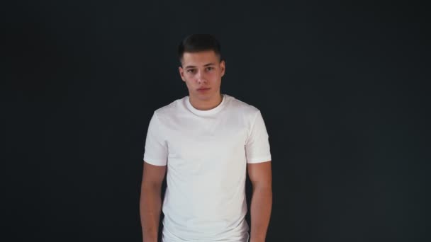 Retrato de joven atractivo y guapo de pie en camisa blanca y se ve en la cámara. Aislado sobre fondo negro — Vídeo de stock