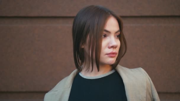 Retrato de una hermosa mujer hipster de raza mixta de moda con chaqueta y jeans. Ella posa frente a la pared marrón — Vídeos de Stock