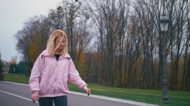 Pembe windstopper eğleniyor genç güzel güzel sarışın hipster kadında kaykay longboard yokuş aşağı yavaş güzel yolda sürme