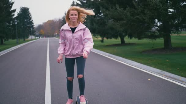 Joven hermosa rubia hipster mujer en rosa windstopper divertirse montar monopatín longboard cuesta abajo en hermosa carretera en cámara lenta — Vídeos de Stock