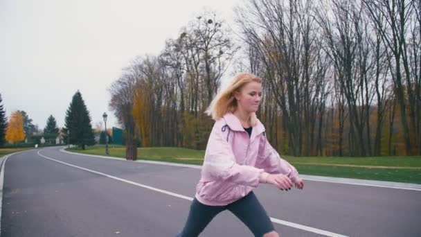 Mladá žena docela krásné blond bokové v růžové windstopper baví na koni skateboard longboard z kopce na krásné silnici v pomalém pohybu — Stock video