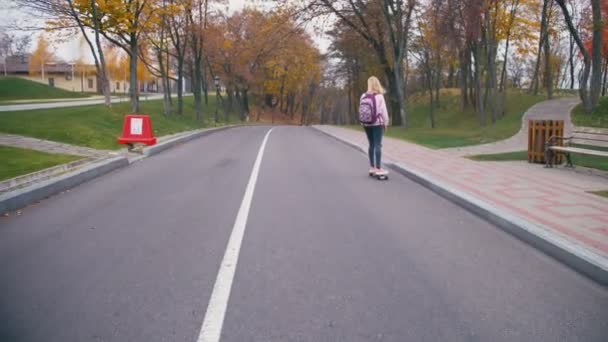 Vrij mooie blonde hipster jongedame in roze windstopper plezier skateboard longboard bergafwaarts rijden op prachtige weg in slow motion — Stockvideo