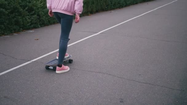 Jeune jolie belle femme blonde hipster en coupe-vent rose s'amusant à monter skateboard longboard descente sur belle route au ralenti — Video