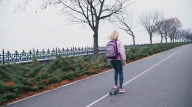 Pembe windstopper eğleniyor genç güzel güzel sarışın hipster kadında kaykay longboard yokuş aşağı yavaş güzel yolda sürme