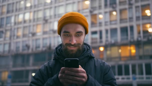 Handsome young man browsing internet on smartphone at city street at evening — Stock Video