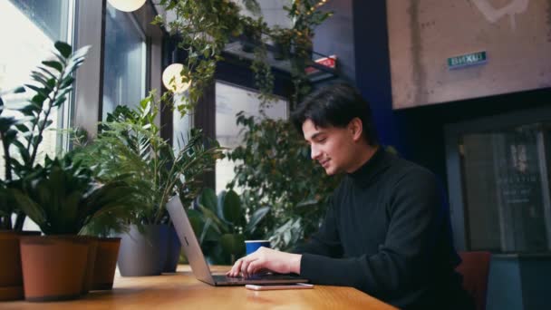 Hombre de raza mixta trabajando con el ordenador portátil y el teléfono inteligente en la cafetería — Vídeos de Stock