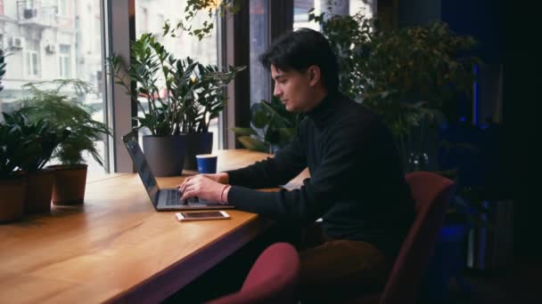 混合种族的人 在咖啡馆与笔记本电脑和智能手机工作 背景中的绿色植物 — 图库视频影像