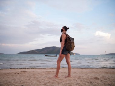 Tıbbi Anti-smog maskesi giymiş bir deniz manzaranın sırt çantası ile kadın gezgin