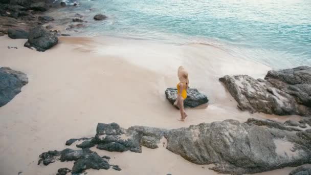 Visão traseira da jovem mulher em maiô amarelo caminhando na bela praia tropical de areia branca . — Vídeo de Stock