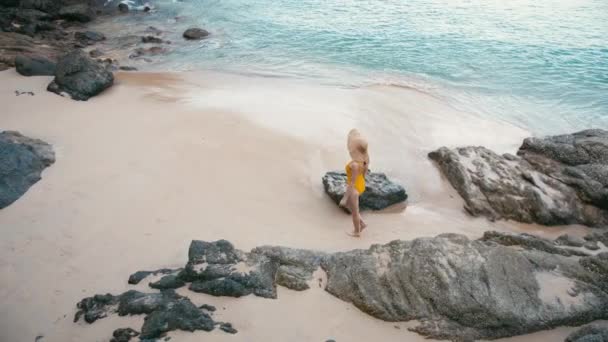 Back view of young woman in yellow swimsuit walking away on the beautiful tropical white sand beach. — Stock Video