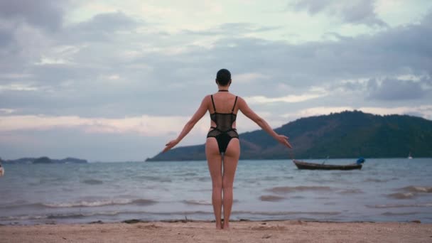 Mujer caucásica practicando yoga en la orilla del mar con traje de baño negro y máscara médica anti-smog — Vídeos de Stock