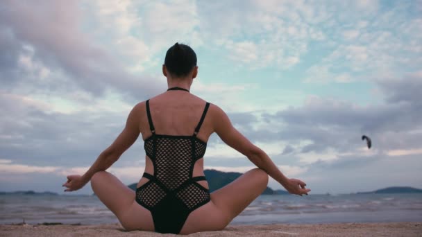 Kaukasische Frau praktiziert Yoga am Meer in schwarzem Badeanzug und medizinischer Anti-Smog-Maske — Stockvideo