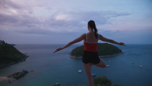 Vrouw praktizerende yoga fitness oefening op hoge plaats met geweldig uitzicht van eiland bij zonsopgang — Stockvideo