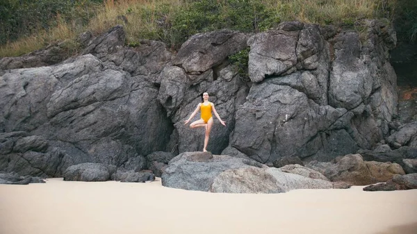 Caucasian woman in yellow smiwsuit practicing yoga fitness exercise at seashore