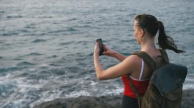 Deniz manzaralı hayran ve sahilde smartphone kullanarak fotoğraf yapma kadın gezgin