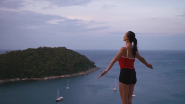 Vrouw praktizerende yoga fitness oefening op hoge plaats met geweldig uitzicht van eiland bij zonsopgang — Stockvideo