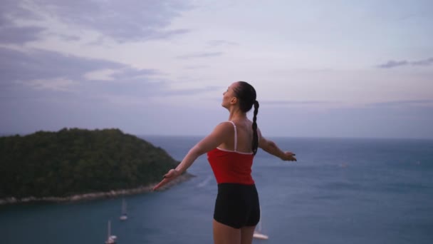 Жінка практикує фізичні вправи на високому місці з дивовижним видом на острів на сході сонця — стокове відео