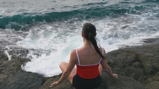 Mujer tranquila practicando yoga ejercicio de fitness en la playa rocosa frente al océano tormentoso — Vídeos de Stock