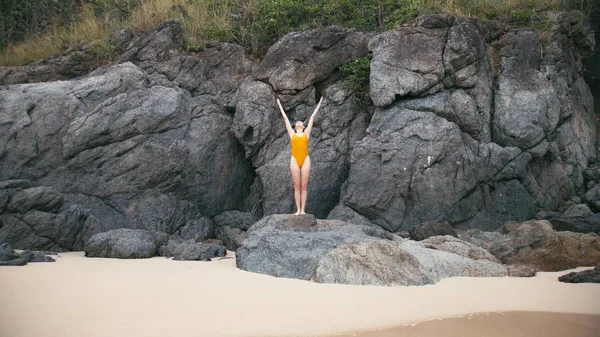 Caucasian woman in yellow smiwsuit practicing yoga fitness exercise at seashore