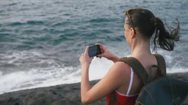 Deniz manzaralı hayran ve sahilde smartphone kullanarak fotoğraf yapma kadın gezgin