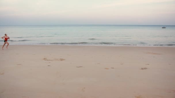 Mulher forte em vermelho correndo na praia exercitando treino cardio em câmera lenta — Vídeo de Stock