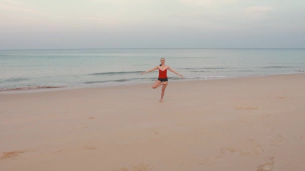 日出前身穿红色西服在海滩练习瑜伽健身运动的女子 — 图库视频影像
