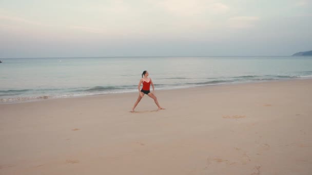 Kobieta w czerwonym smiwsuit praktykowania jogi fitness ćwiczenia na plaży przed wschodem słońca — Wideo stockowe