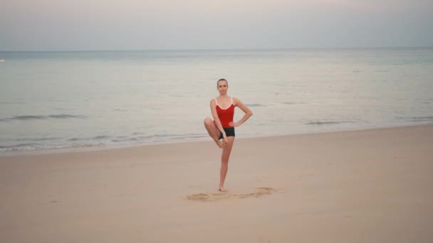 Frau im roten Smiwsuit praktiziert Yoga-Fitness-Übung am Strand vor Sonnenaufgang — Stockvideo