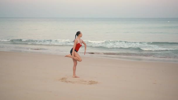 日の出前にビーチで赤 smiwsuit 練習ヨガ ・ フィットネスの女性のエクササイズします。 — ストック動画