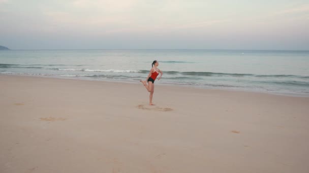 Kobieta w czerwonym smiwsuit praktykowania jogi fitness ćwiczenia na plaży przed wschodem słońca — Wideo stockowe