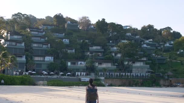 Bella donna viaggiatore con zaino a piedi dalla spiaggia al resort di lusso all'alba — Video Stock