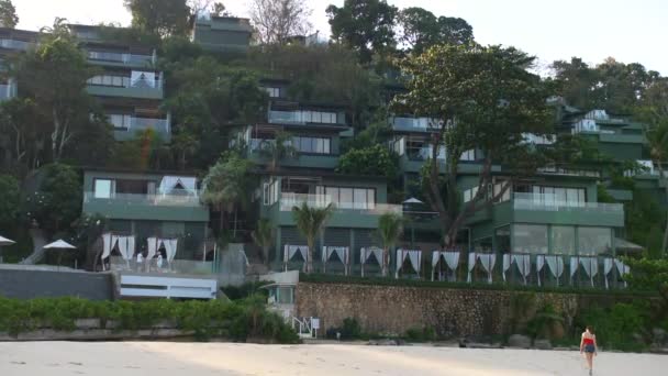 Hermosa mujer en rojo caminando por la playa hasta el hotel spa de lujo al amanecer — Vídeos de Stock