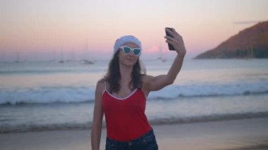 Plaj tatil selfie fotoğrafta kırmızı santa şapka eğlenceli kadında. Yaz tatil kız mutlu smartphone kamera kendi kendine portre onun seyahat etmek tatiller bozulmamış Cennet plaj üzerinde alarak.