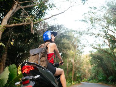 Mavi kask palmiye ağaçları ile orman yolda scooter motosiklet sürüş kadında. Tropikal seyahat ve motosiklet taşıma