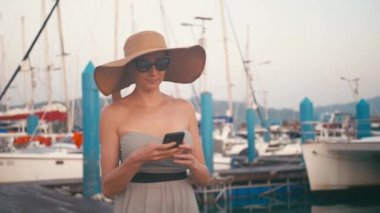 Marina iskele yatlar, arka plan ile yürüyüş onun smartphone kullanarak elbiseli şık Bayan
