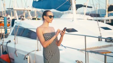 Marina iskele yatlar, arka plan ile onun smartphone kullanarak elbiseli şık Bayan