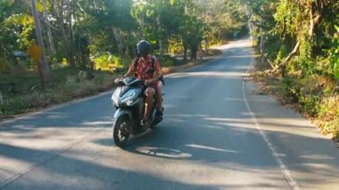 Genç güzel turistik çift ile kask giymiş bir scooter üzerinde ormana gidiyor. Seyahat, özgürlük, mutluluk, tatil, balayı konsepti.