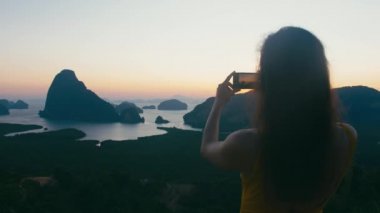 Kadın turist ünlü dönüm noktası Phang Nga sunrise defne, smartphone kullanarak fotoğraf yapar