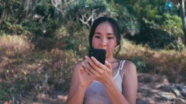 Genç mutlu güzel Asyalı kadın telefon açık havada doğada kullanarak spor giyim