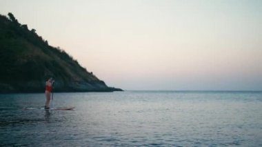 Kadın kürek kurulu bir koyda Sup ayağa batımında üzerinde kırmızı mayo