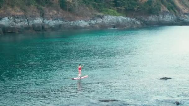 在日落时, 身穿红色泳衣的妇女在海湾上站起立划桨板 — 图库视频影像